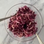 Red and white cabbage salad in a serving bowl with two spoons