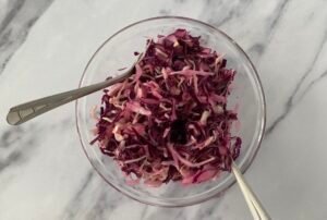 Red and white cabbage salad in a serving bowl with two spoons