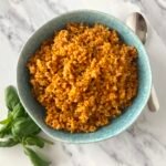 Bowl of tomato and bulgur pilaf served with fresh basil leaves