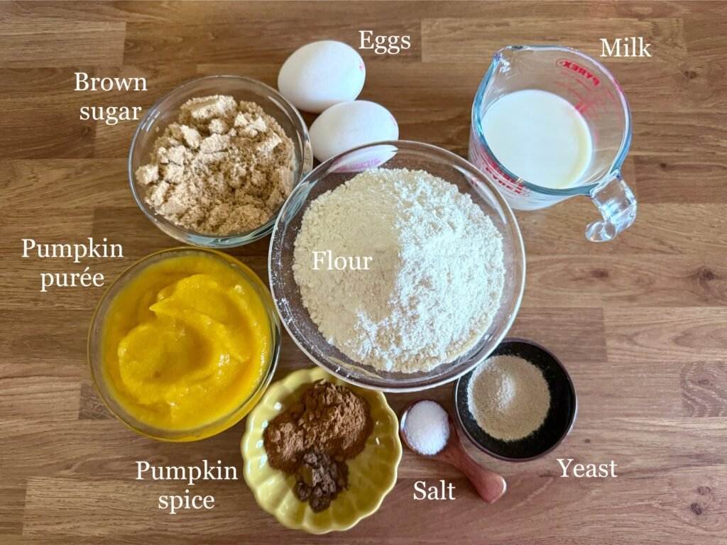 ngredients for pumpkin and cinnamon swirls laid out on a wooden countertop, including flour, pumpkin purée, cinnamon, brown sugar, butter, and cream cheese, arranged to highlight the baking essentials.