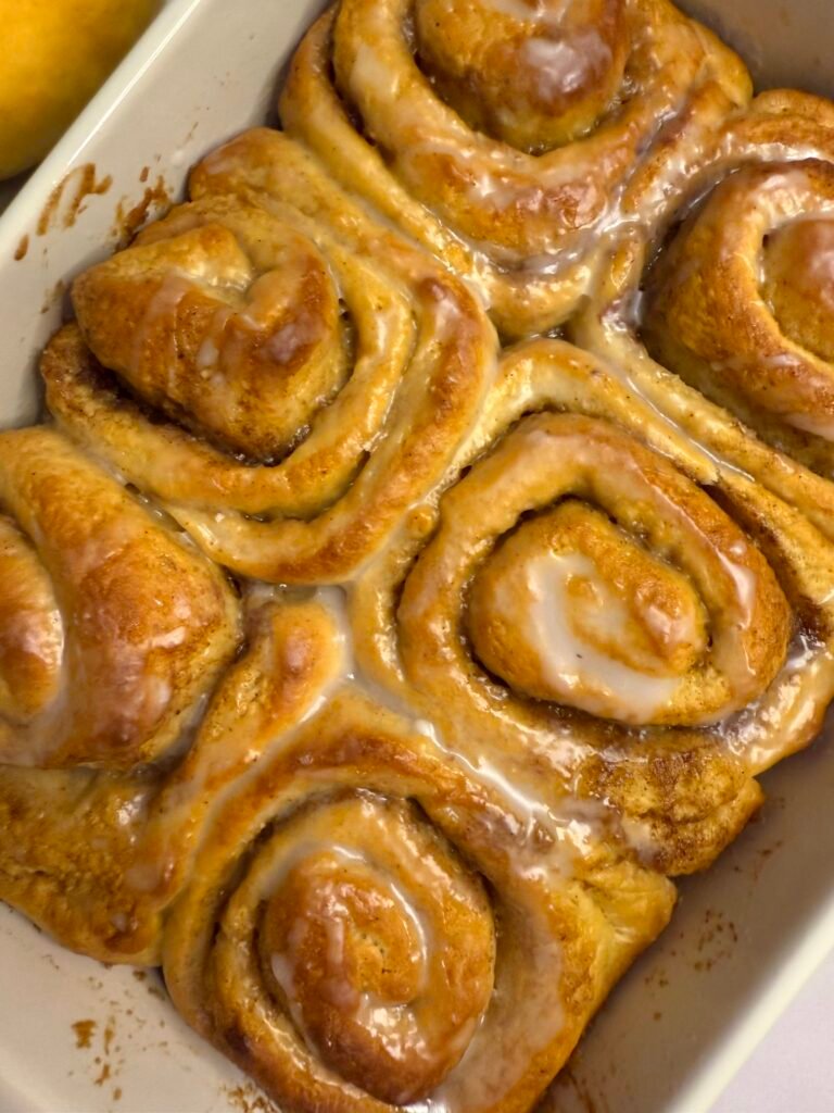 A tray of freshly baked pumpkin and cinnamon swirls, golden and fluffy, topped with a light drizzle of cream cheese glaze, showcasing the swirled layers of pumpkin filling and cinnamon.