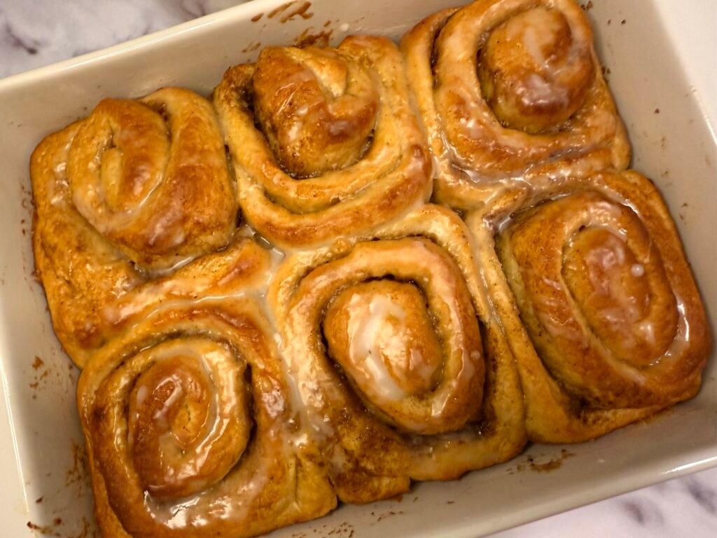 A tray of freshly baked pumpkin and cinnamon swirls, golden and fluffy, topped with a light drizzle of cream cheese glaze, showcasing the swirled layers of pumpkin filling and cinnamon.