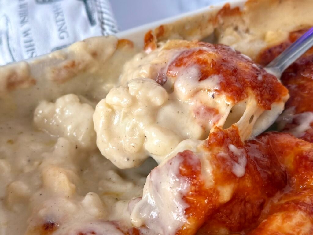 A close-up of golden-brown cauliflower cheese in a baking dish, topped with a crispy cheese and breadcrumb crust.