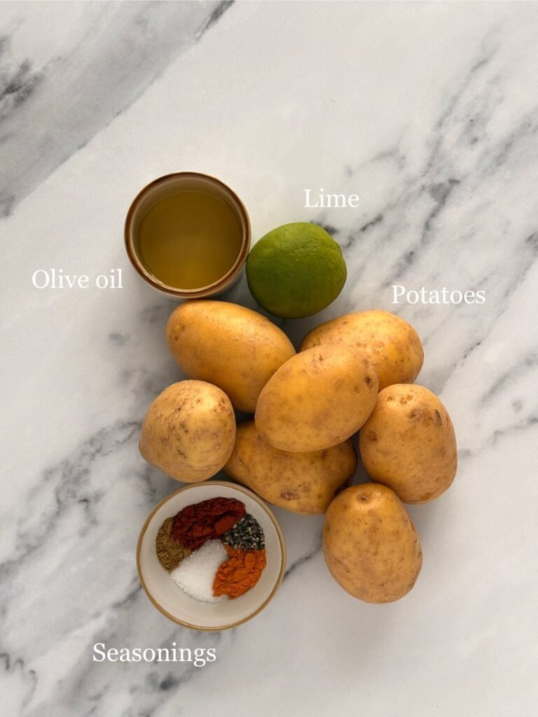 Raw potatoes, a bottle of olive oil, and small bowls of paprika, turmeric, cumin, black pepper, and lime.