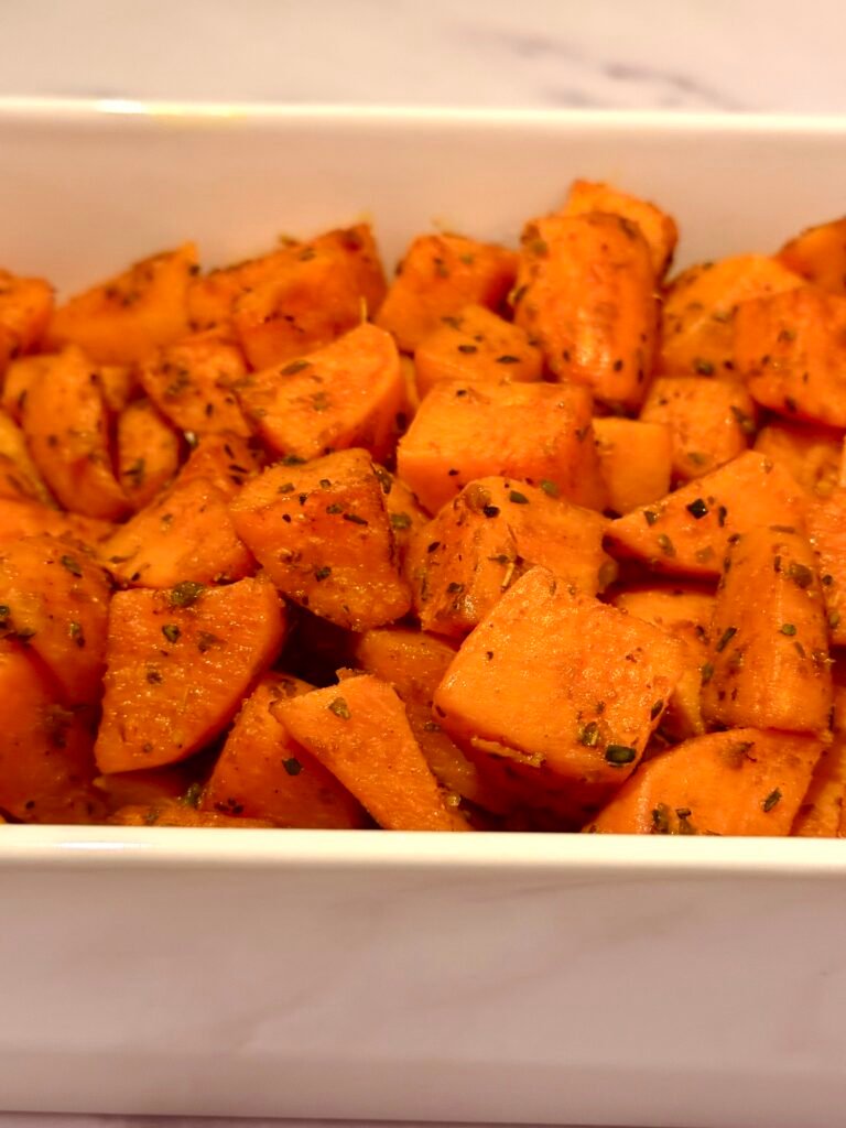 A baking sheet filled with perfectly roasted sweet potato cubes, golden brown and caramelized, garnished with fresh herbs.