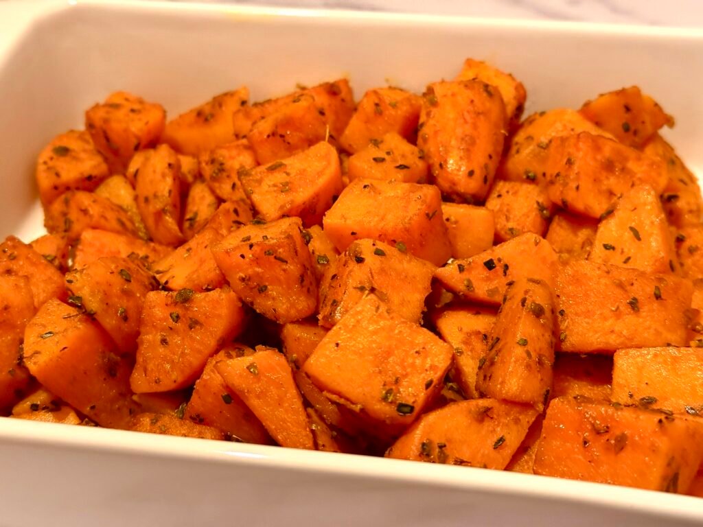 A baking sheet filled with perfectly roasted sweet potato cubes, golden brown and caramelized, garnished with fresh herbs.