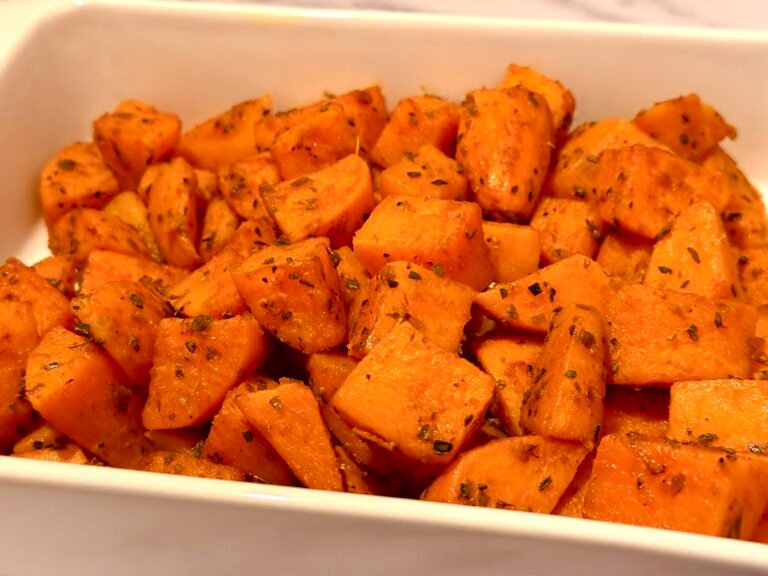 A baking sheet filled with perfectly roasted sweet potato cubes, golden brown and caramelized, garnished with fresh herbs.