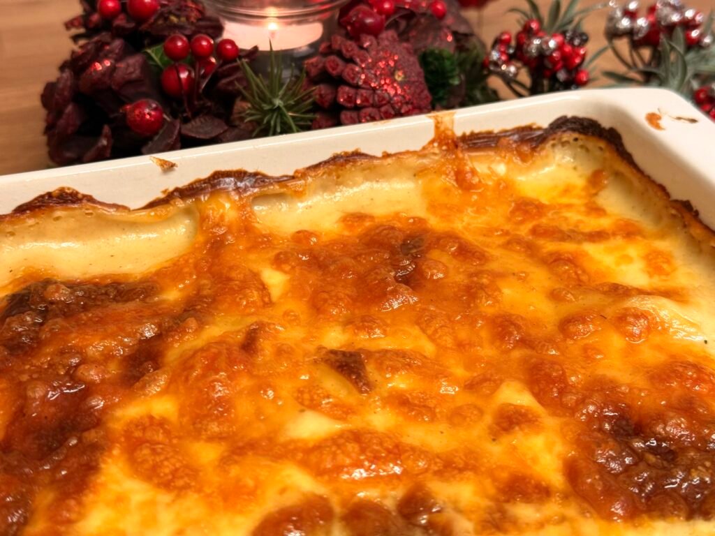 Golden and bubbly Potato Dauphinoise served in a white baking dish, garnished with fresh herbs.