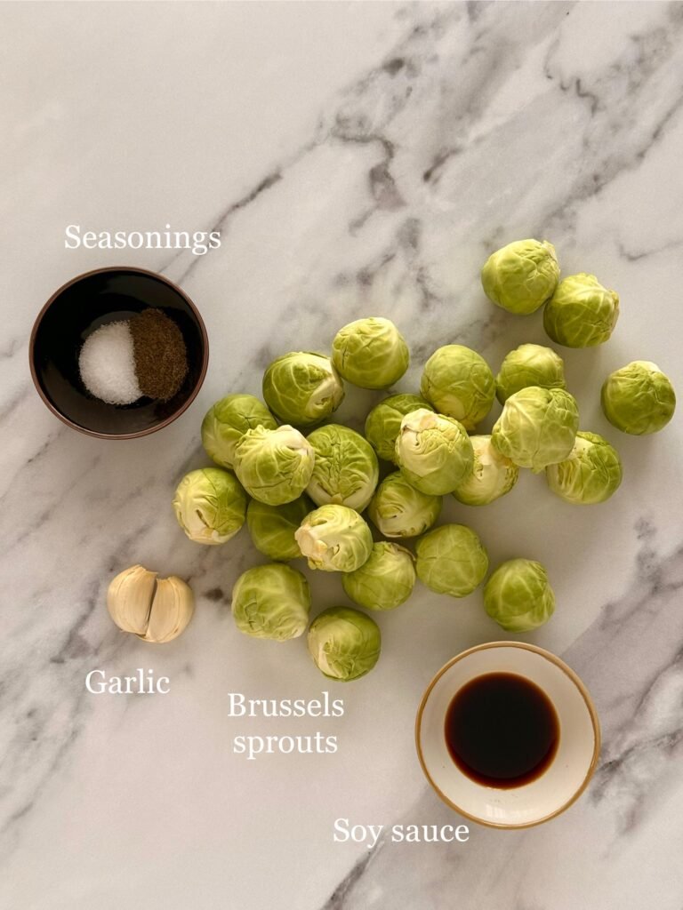 Fresh Brussels sprouts, soy sauce, garlic cloves, salt, and pepper arranged on a countertop before cooking.