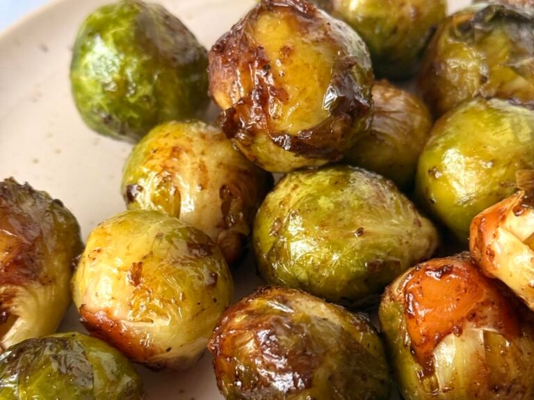 A plate of golden-brown sautéed Brussels sprouts, served on a cream ceramic plate, a perfect side for a roast dinner.