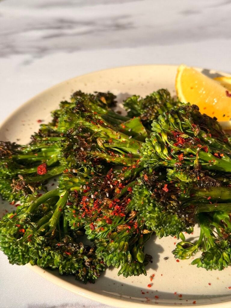 Close-up shot of charred broccoli florets with crispy edges and bright lemon slices.